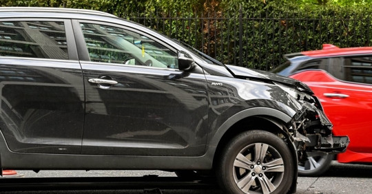 Car accident scene between a black sedan and a red sedan.