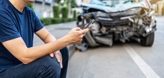 man on phone in front of damaged car